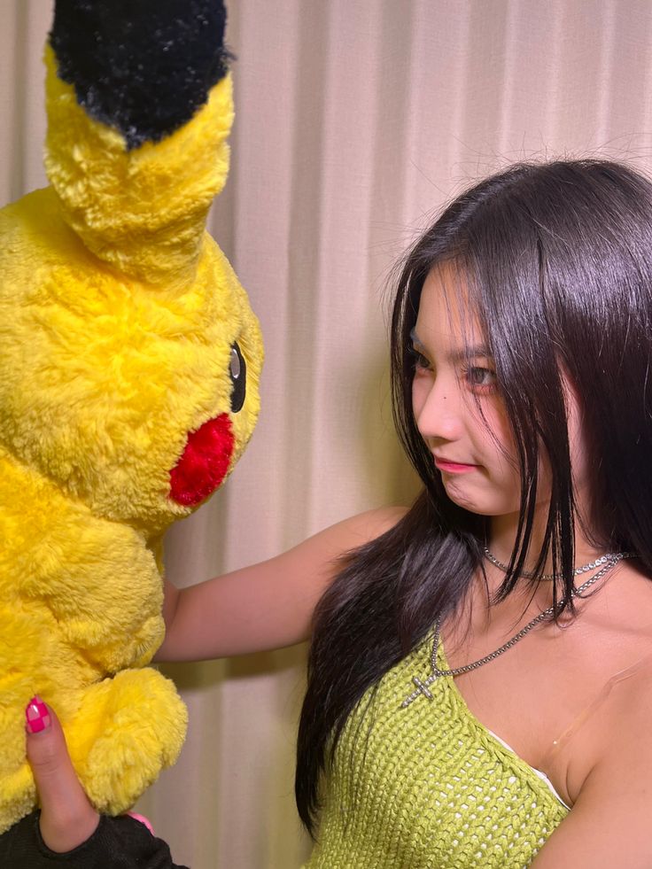 a young woman holding onto a stuffed toy pikachu and smiling at the camera