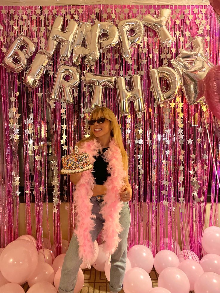 a woman standing in front of balloons and streamers with a cake on her plate