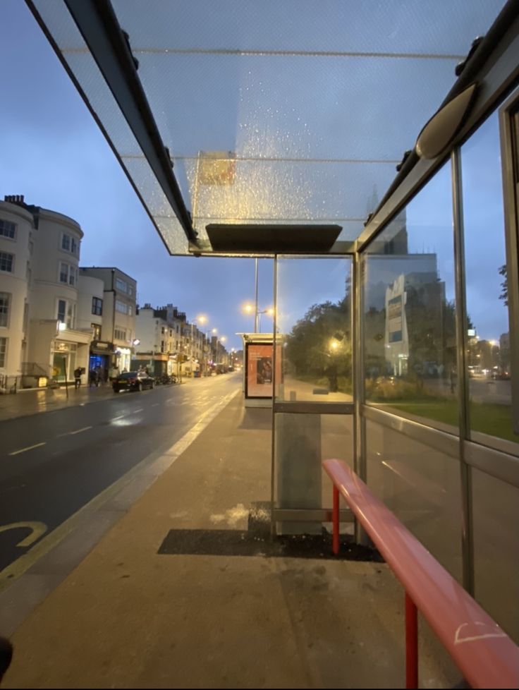 an empty bus stop at night with the lights on and buildings in the background,