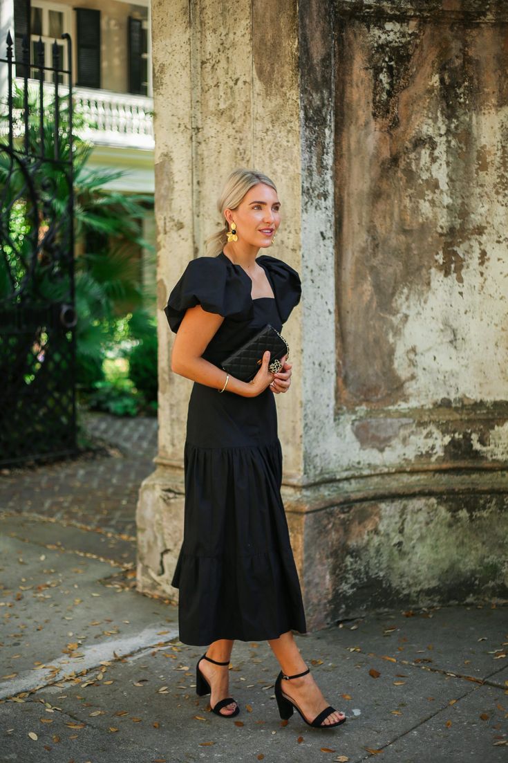 a woman standing in front of an old building wearing a black dress and high heels