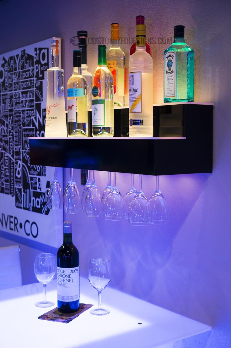 several bottles and glasses on a shelf in a room with purple lighting behind them,