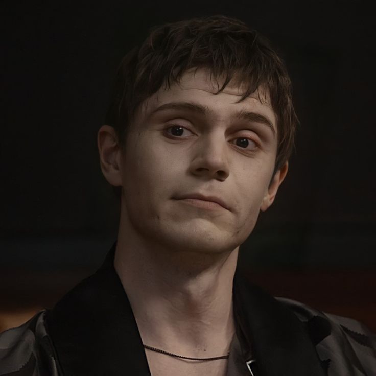 a close up of a person wearing a black shirt and silver necklace with an evil look on his face
