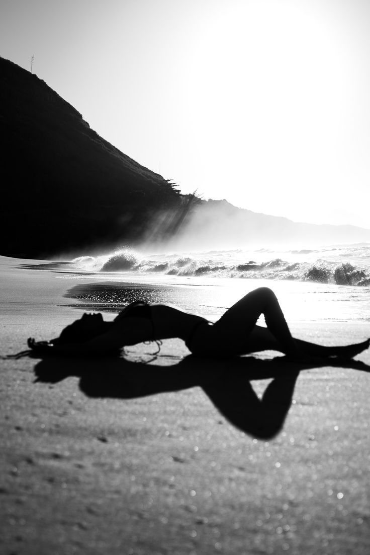 a woman laying on top of a sandy beach next to the ocean with her legs spread out
