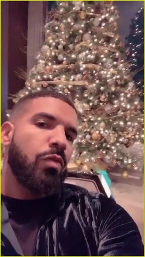 a man with a beard is sitting in front of a christmas tree and looking at the camera