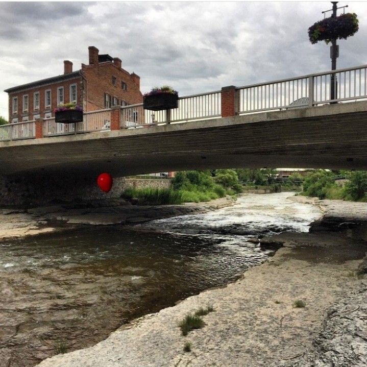 a red ball is floating in the water under a bridge over a small river that runs between two buildings