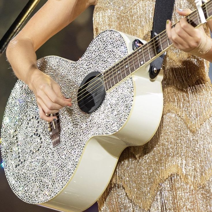 a woman in a gold dress holding a guitar and singing into a microphone on stage