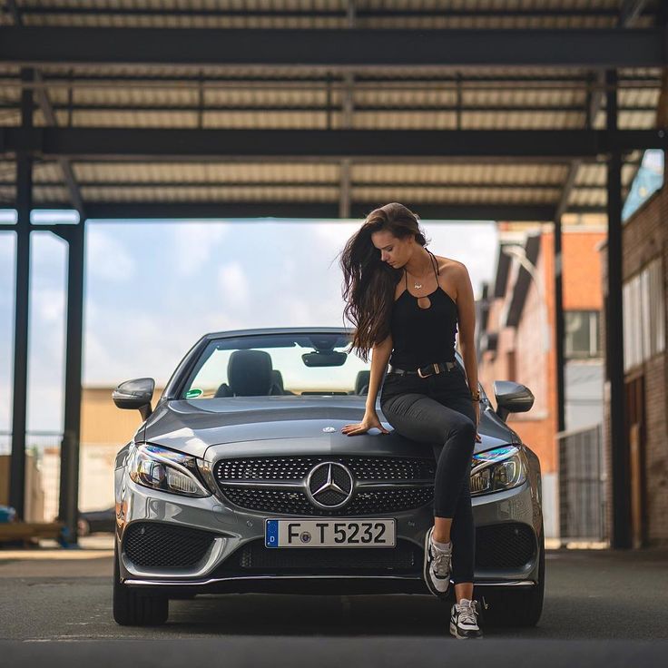 a woman sitting on the hood of a mercedes benz s - class car in front of a garage