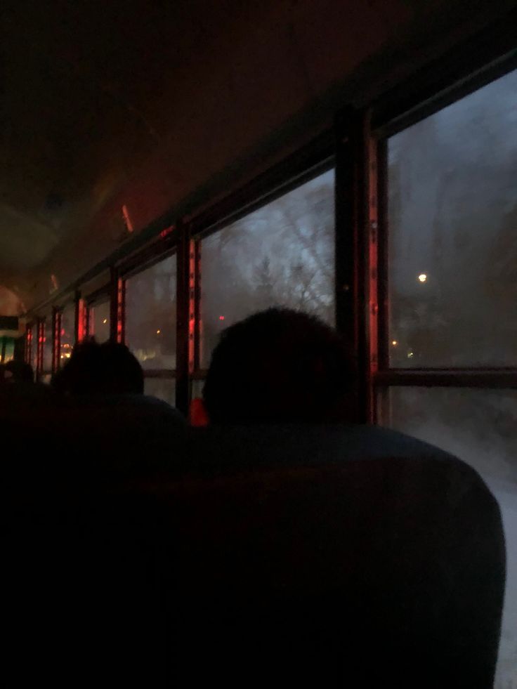 some people are sitting on a bus at night and one is looking out the window