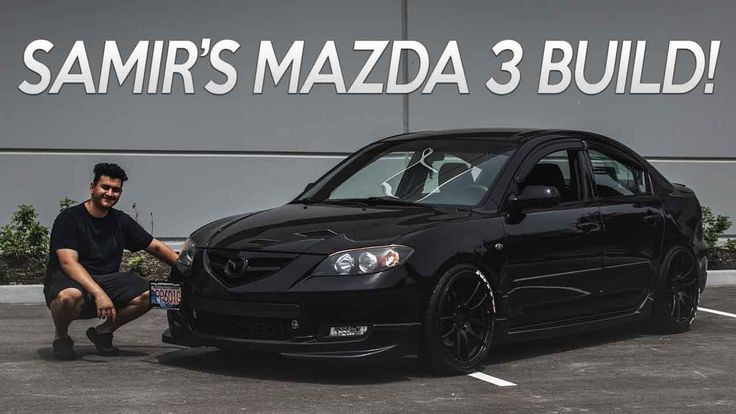 a man kneeling down next to a black car in front of a large sign that says sam's mazda 3 build