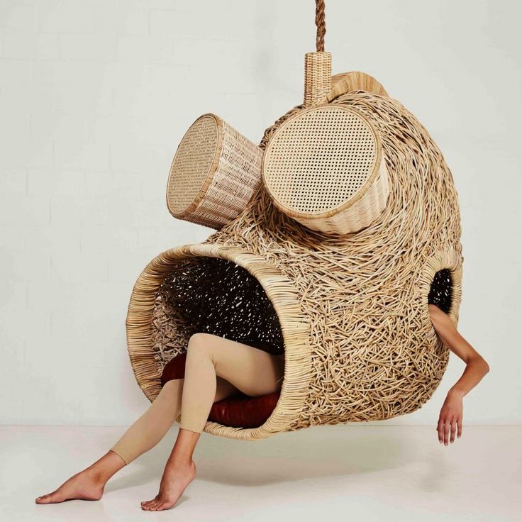 a woman laying on the ground in front of a hanging chair made out of wicker