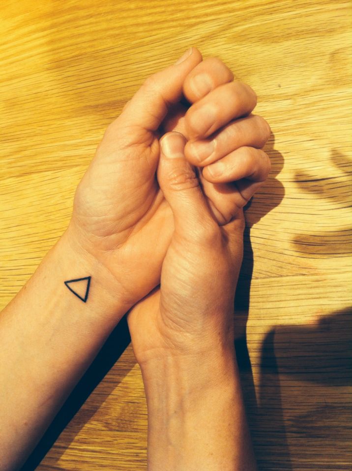 two hands holding each other with a small triangle tattoo on the wrist and one hand