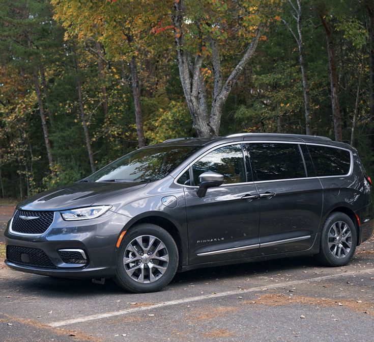 a grey minivan parked in a parking lot next to trees and leaves on the ground