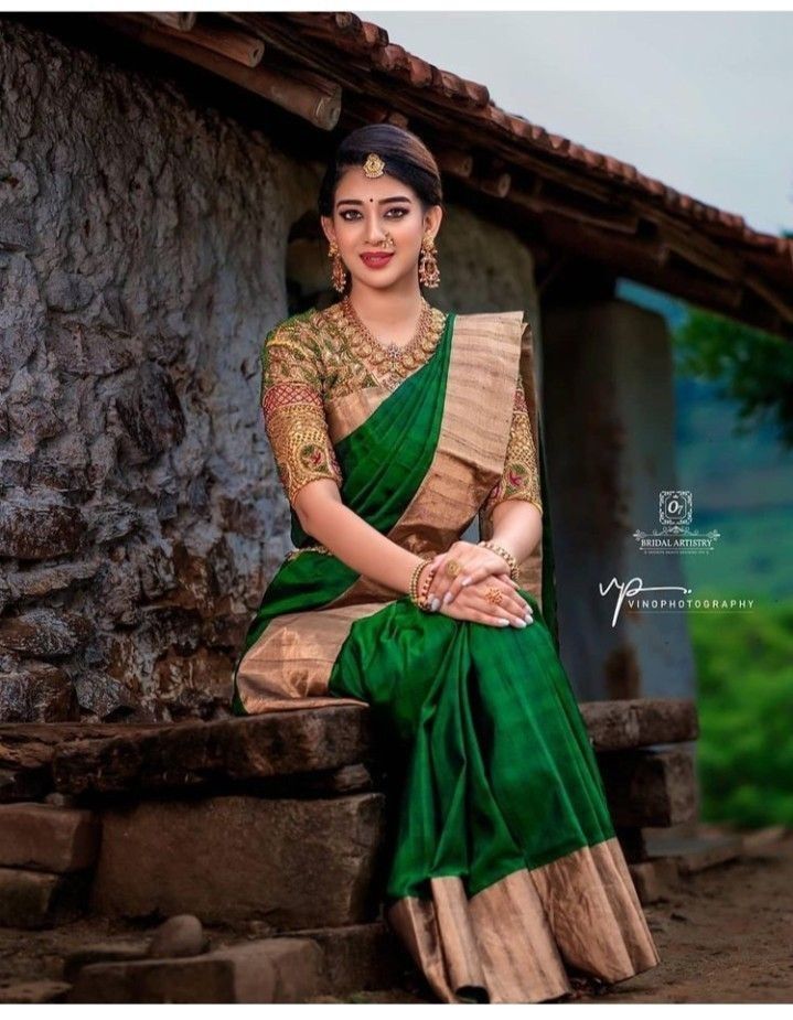 a woman in a green and gold sari sitting on a stone wall with her hands folded