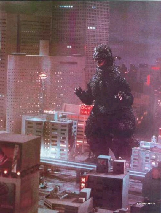 godzilla standing on top of a building with city lights in the backgrouund