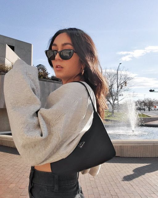 a woman wearing sunglasses and carrying a black handbag in front of a water fountain