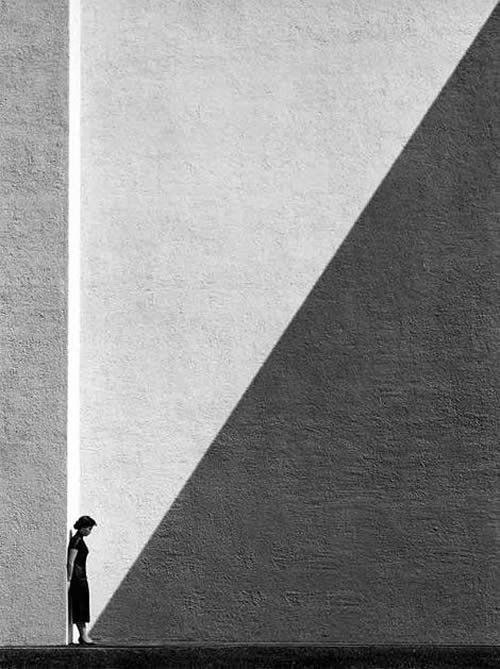 a person standing in front of a building with a shadow on the wall behind them