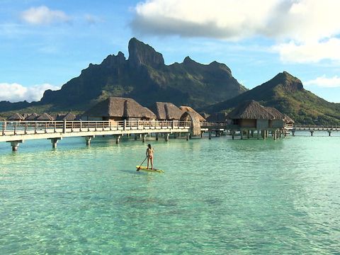 a person on a surfboard in the water near some mountains and houses with thatched roofs