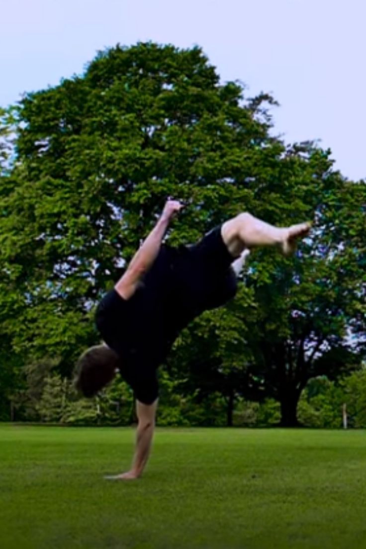 a man is doing a handstand on the grass with trees in the background