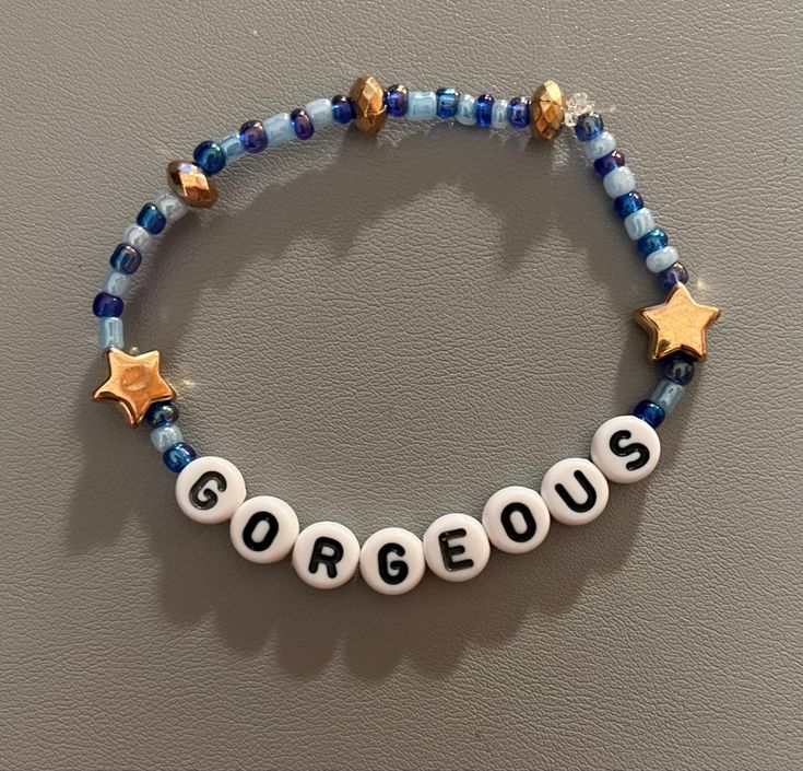 a beaded bracelet with the word gorgeous written on it and two gold star charms