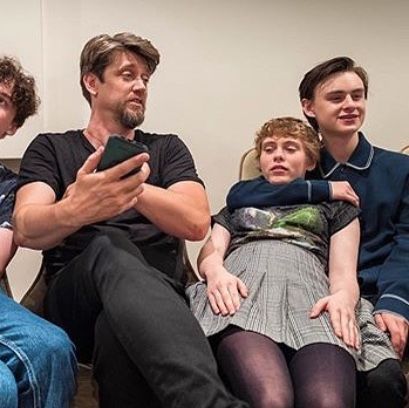 four people sitting on a couch looking at a cell phone with one person holding the other's head