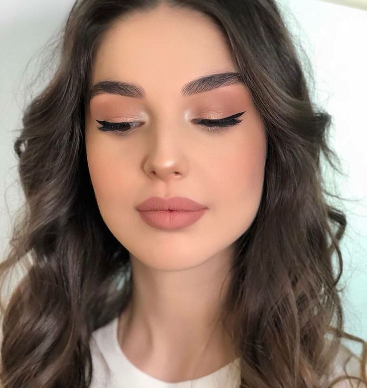 a woman with long dark hair and brown eyeshadow, wearing a white top