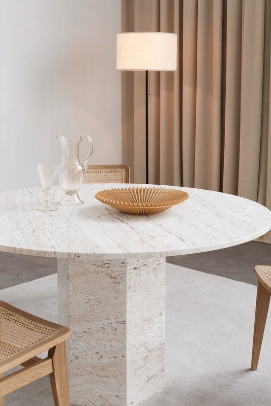 a white marble dining table with two chairs and a vase on the top, in front of a beige curtained window