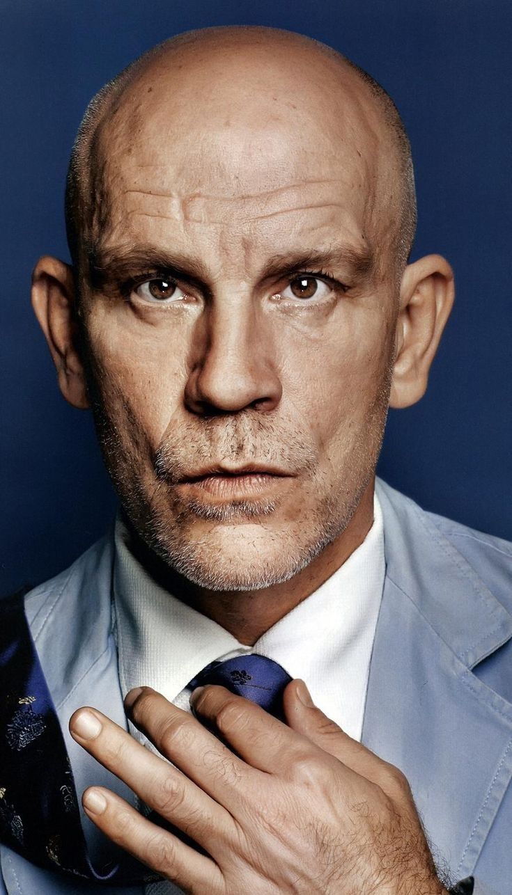 a bald man in a blue shirt and tie is posing for a photo with his hands on his chest