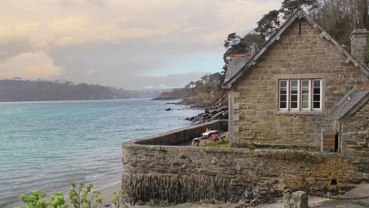 an old stone house sitting on the edge of a body of water