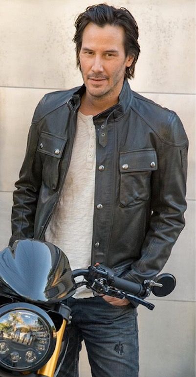 a man standing next to a motorcycle wearing a leather jacket and jeans with his hands in his pockets