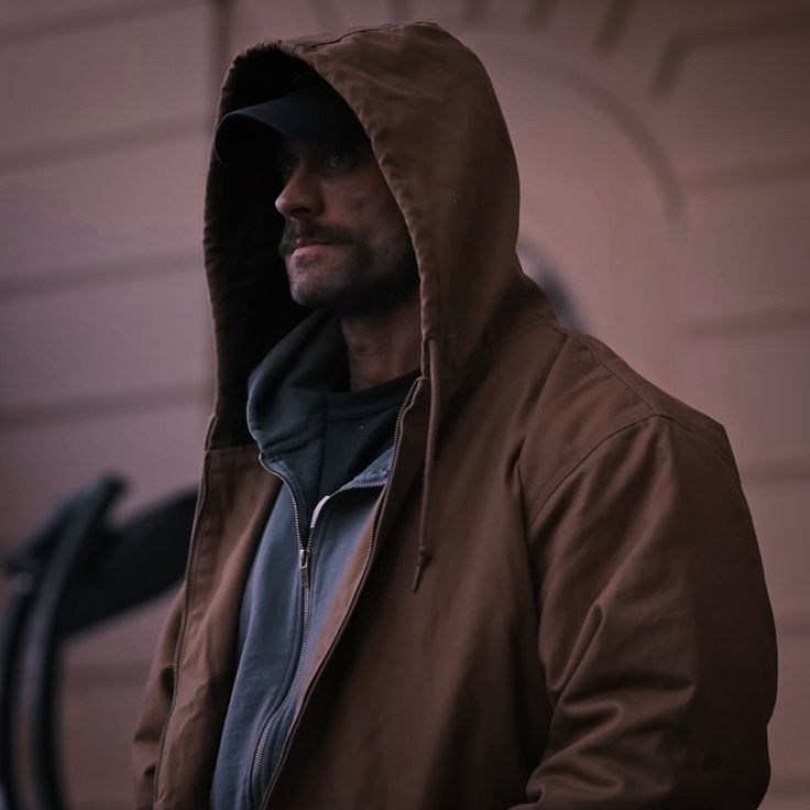 a man wearing a brown jacket and hoodie standing in front of a garage door