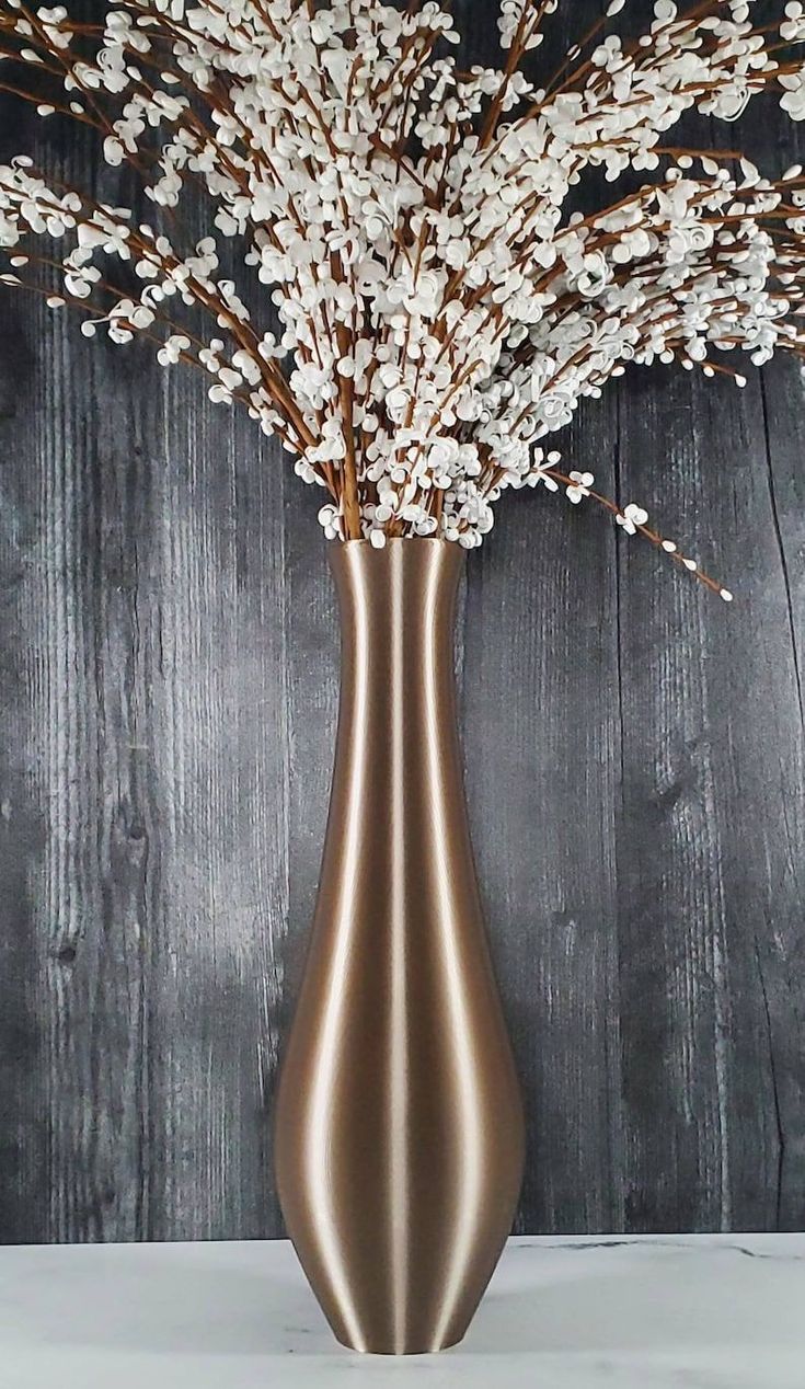 a vase filled with white flowers sitting on top of a wooden table next to a wall