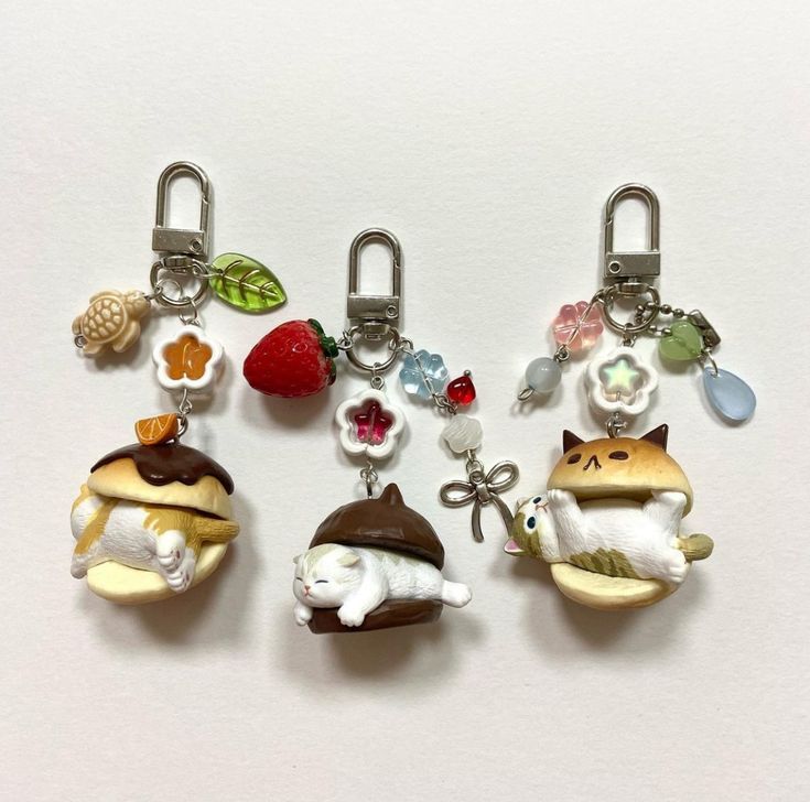 four different key chains with animals and fruits hanging from each one's sides on a white surface