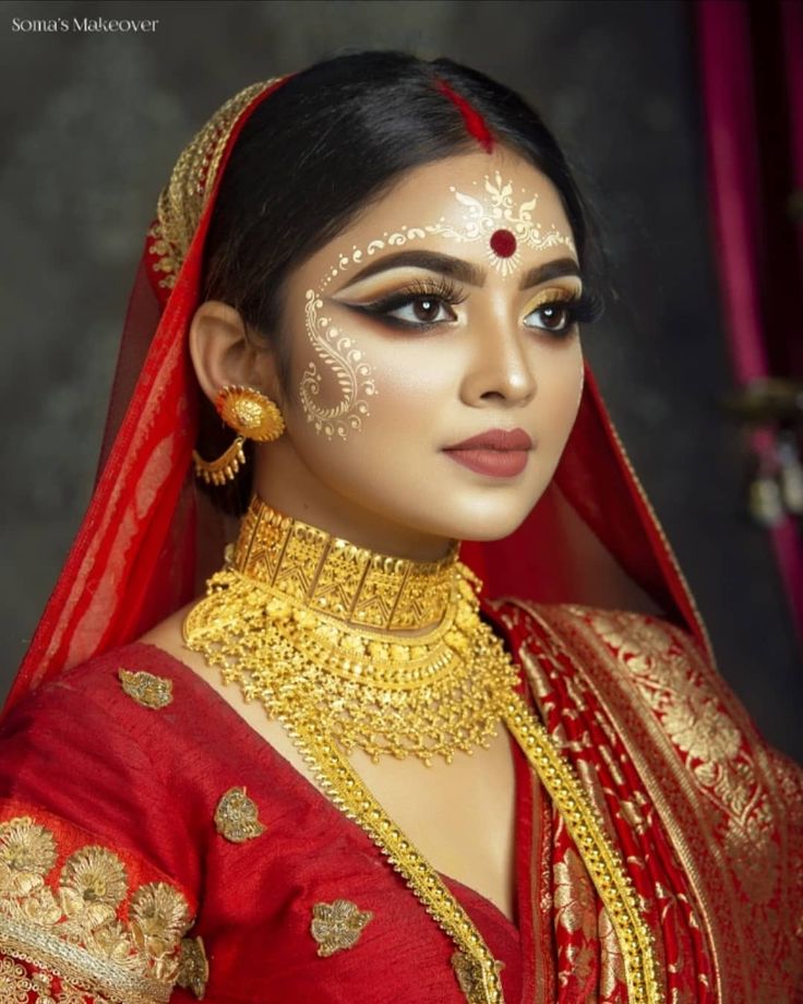 a woman wearing a red and gold bridal outfit with jewelry on her head, in front of a dark background