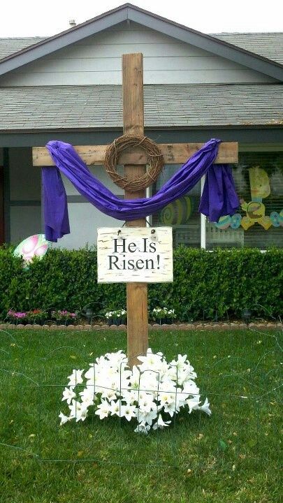 a wooden cross sitting in front of a house with purple and white decorations around it