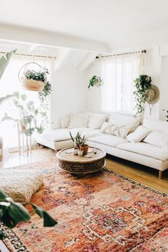 a living room with white couches, rugs and potted plants on the windowsill