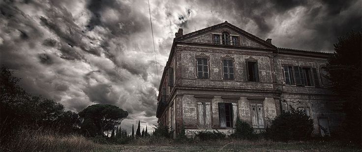 an old abandoned house sitting in the middle of a field under a cloudy sky with dark clouds