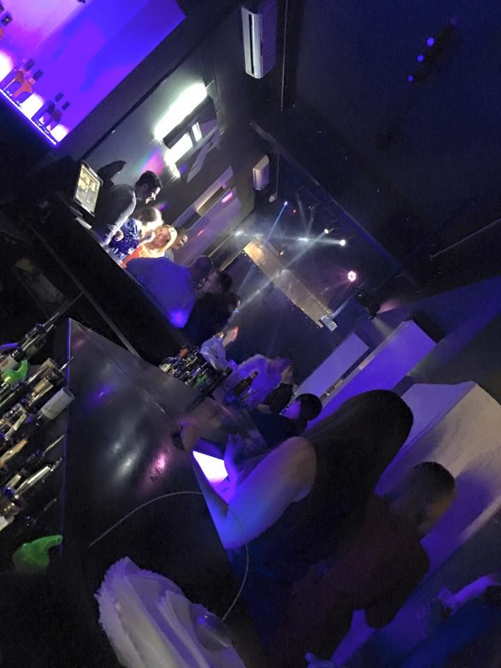 people are sitting at tables in a dimly lit room with purple lighting on the walls