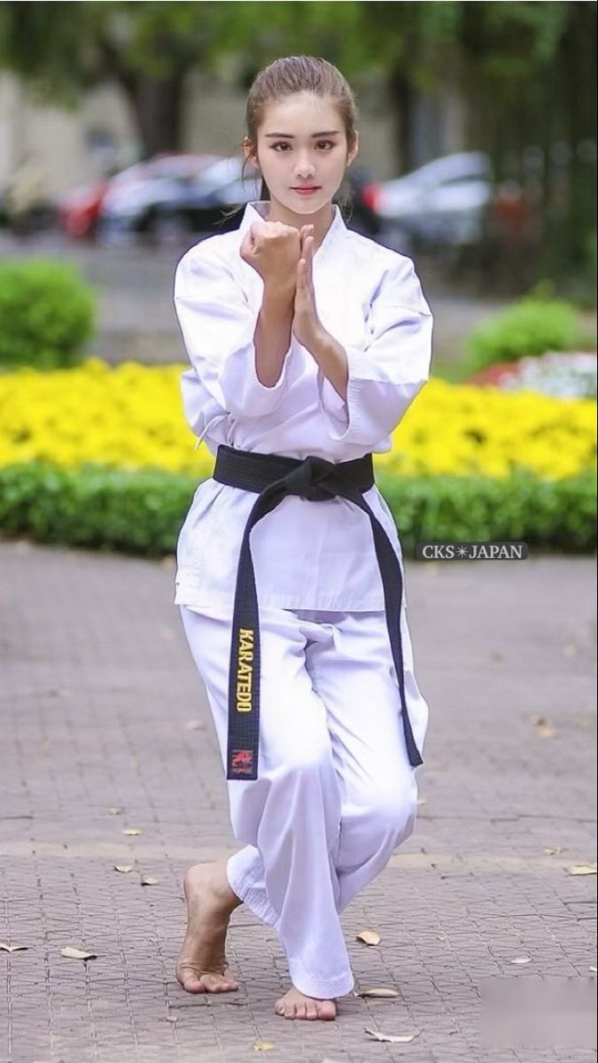 a young woman is practicing karate moves in the park, with yellow flowers behind her