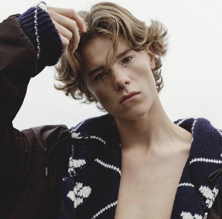 a young man with curly hair and no shirt is posing for the camera while wearing a cardigan