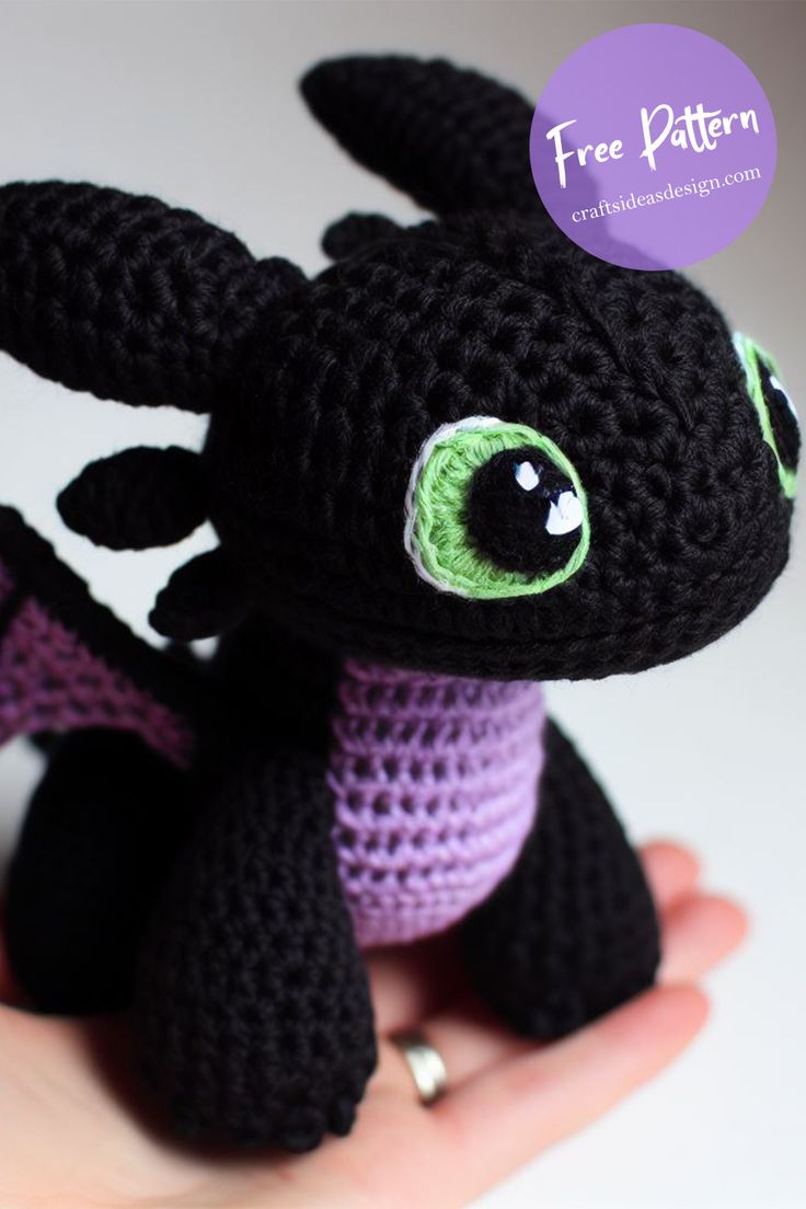 a small crocheted black dragon with green eyes sitting on someone's hand