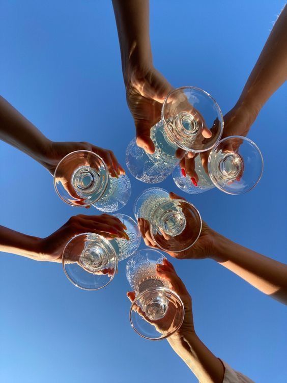 several people are holding wine glasses in the middle of a circle on a sunny day