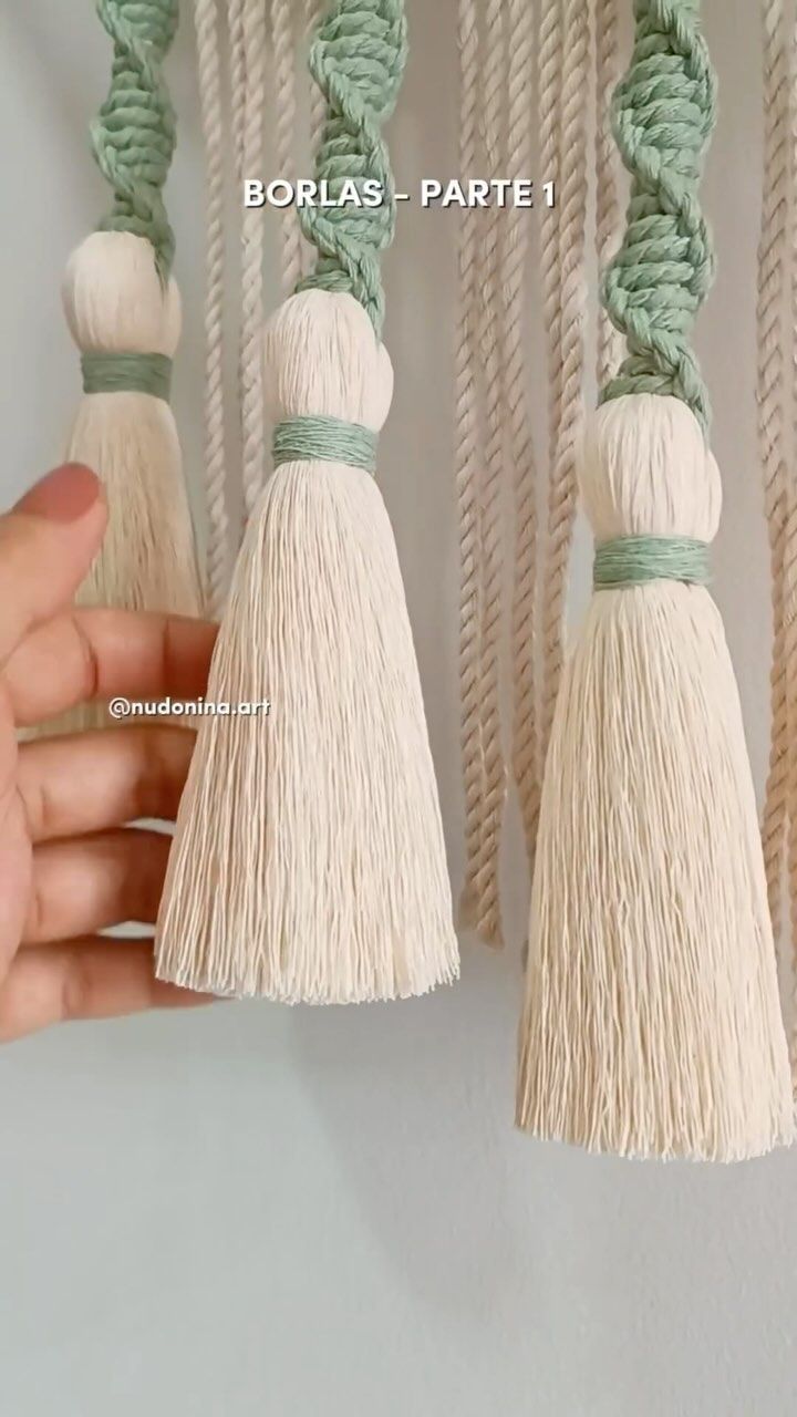 two white tassels with green cords hanging from the ceiling in front of a person's hand