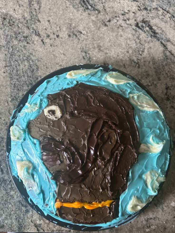 a cake with chocolate frosting and blue icing on a marble counter top next to a knife