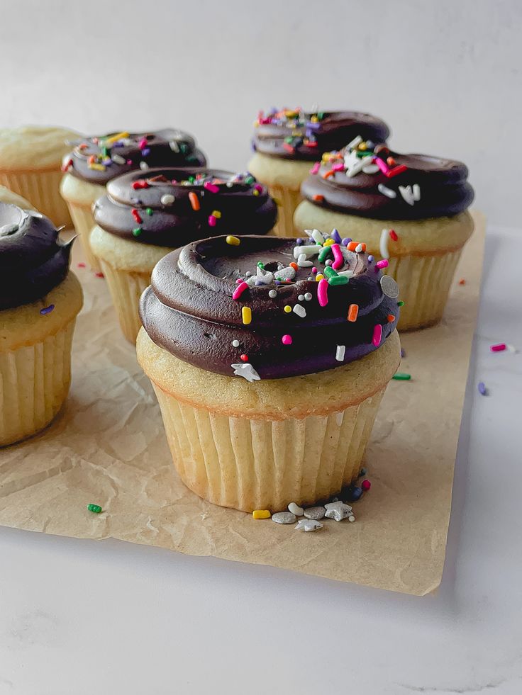 several cupcakes with chocolate frosting and sprinkles on a piece of paper