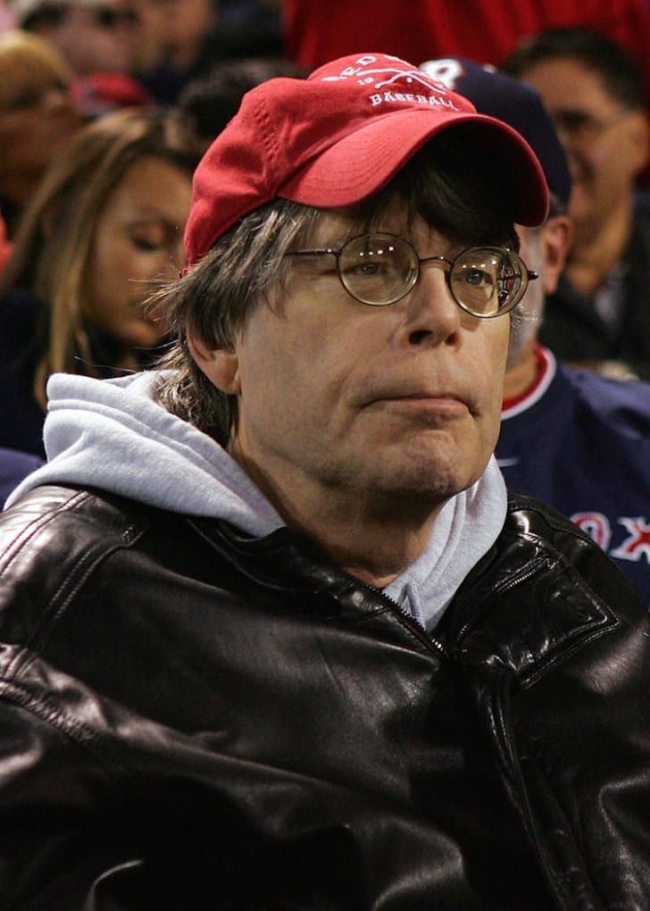 a man with glasses and a red hat is sitting in the stands at a baseball game