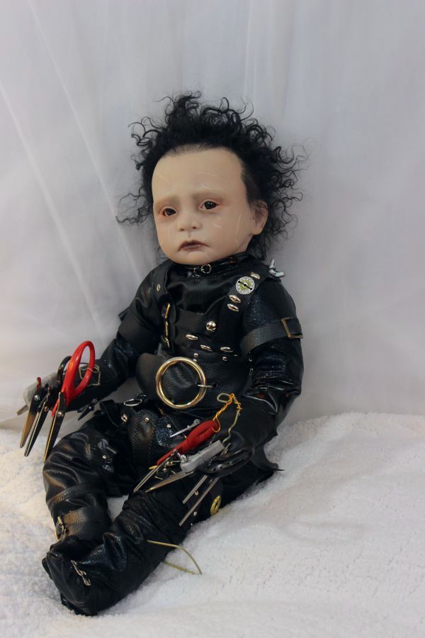 a baby doll with black hair sitting on a white surface holding scissors and pliers