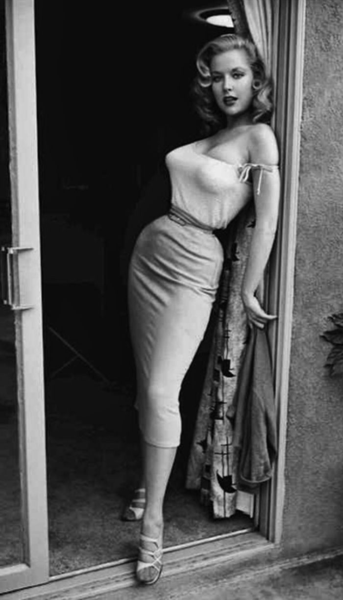 an old photo of a woman standing in front of a door with her hands on her hips