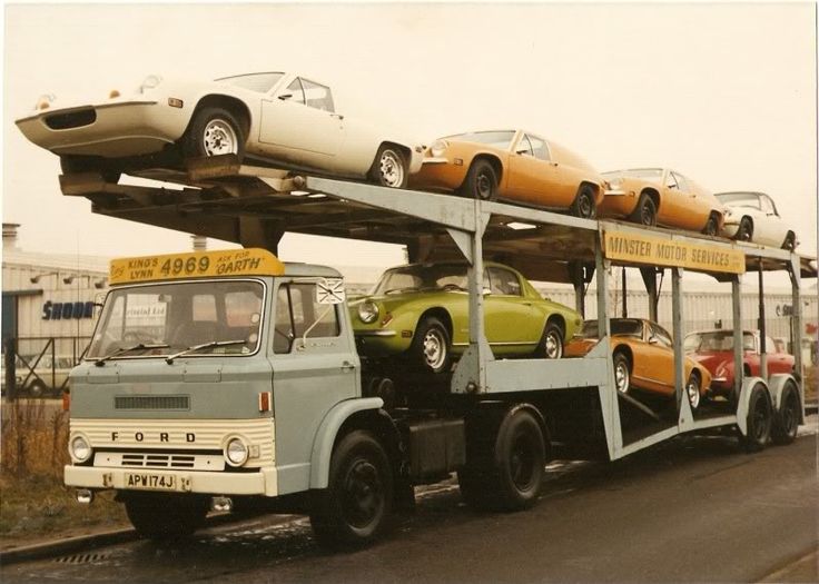 two cars are on top of a truck with three other cars in the back ground