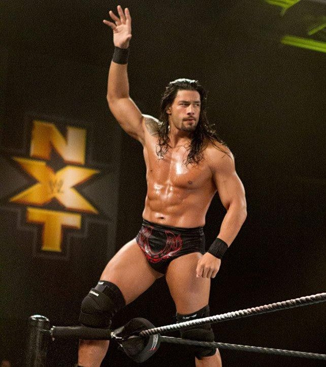 a man with no shirt standing on top of a wrestling ring holding his hand up in the air