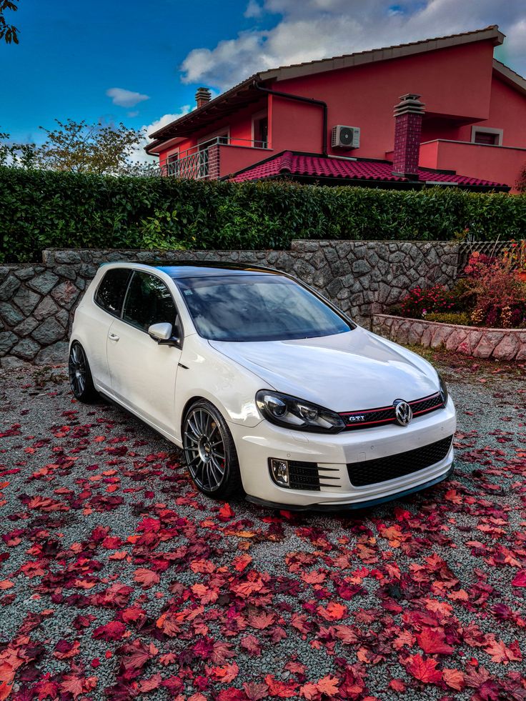 a white car parked in front of a red house with leaves on the ground next to it